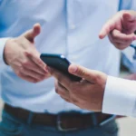 two men looking at their cell phones one in the other is pointing to the screen